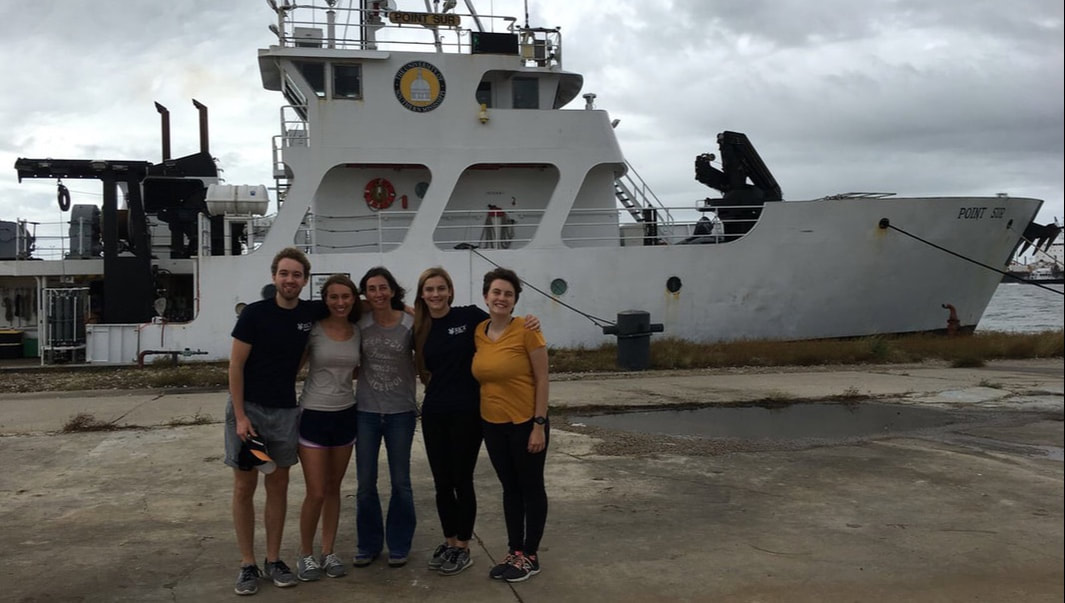 Five members of the Correa Lab stand in front of a research vessel. In the background, the sky is grey and cloudy.